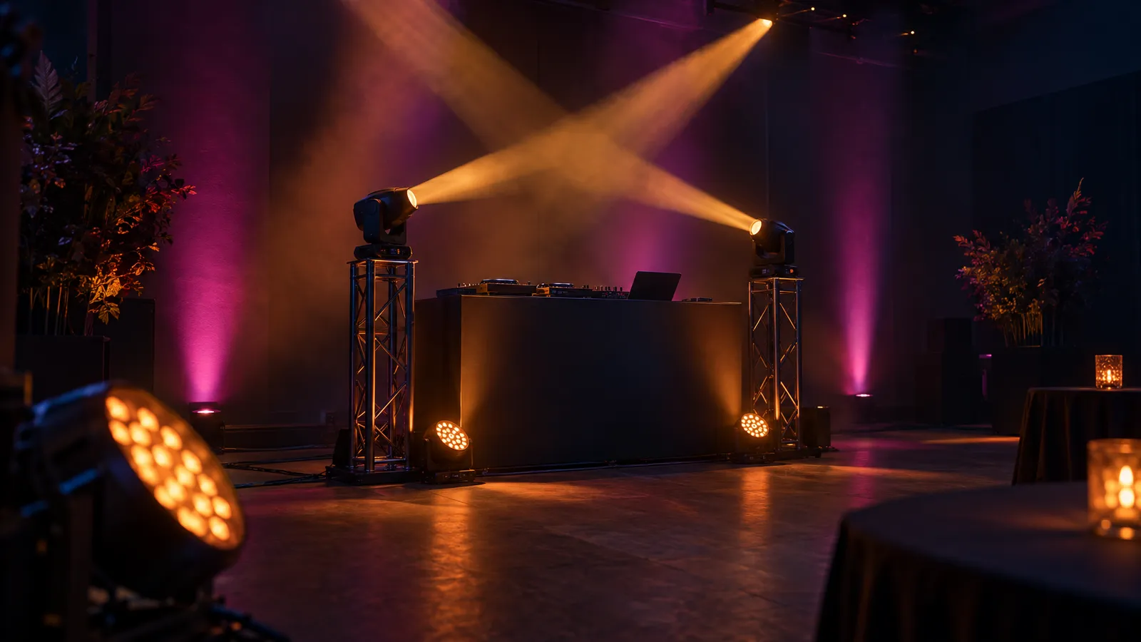 A DJ booth with amber par washes, magenta uplights and moving-head beams visible through light haze in a dark event venue.